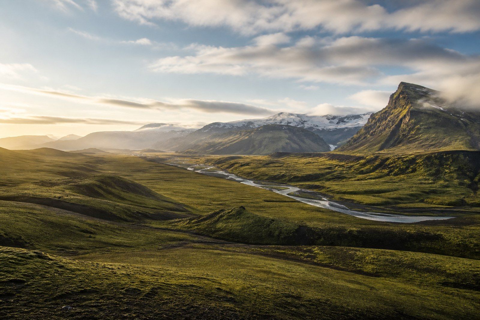 Moss-covered Icelandic valley with a glacial river and distant mountains