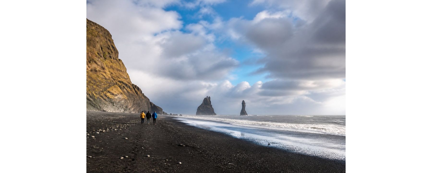 Three travelers walking together on an Icelandic black-sand beach