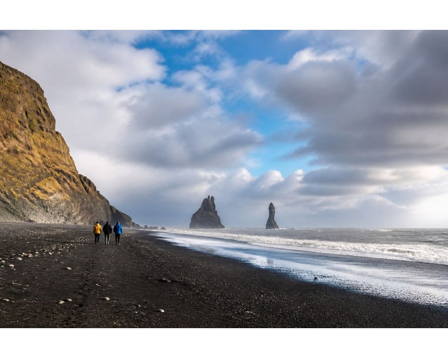 Three travelers walking along an expansive black-sand beach in Iceland