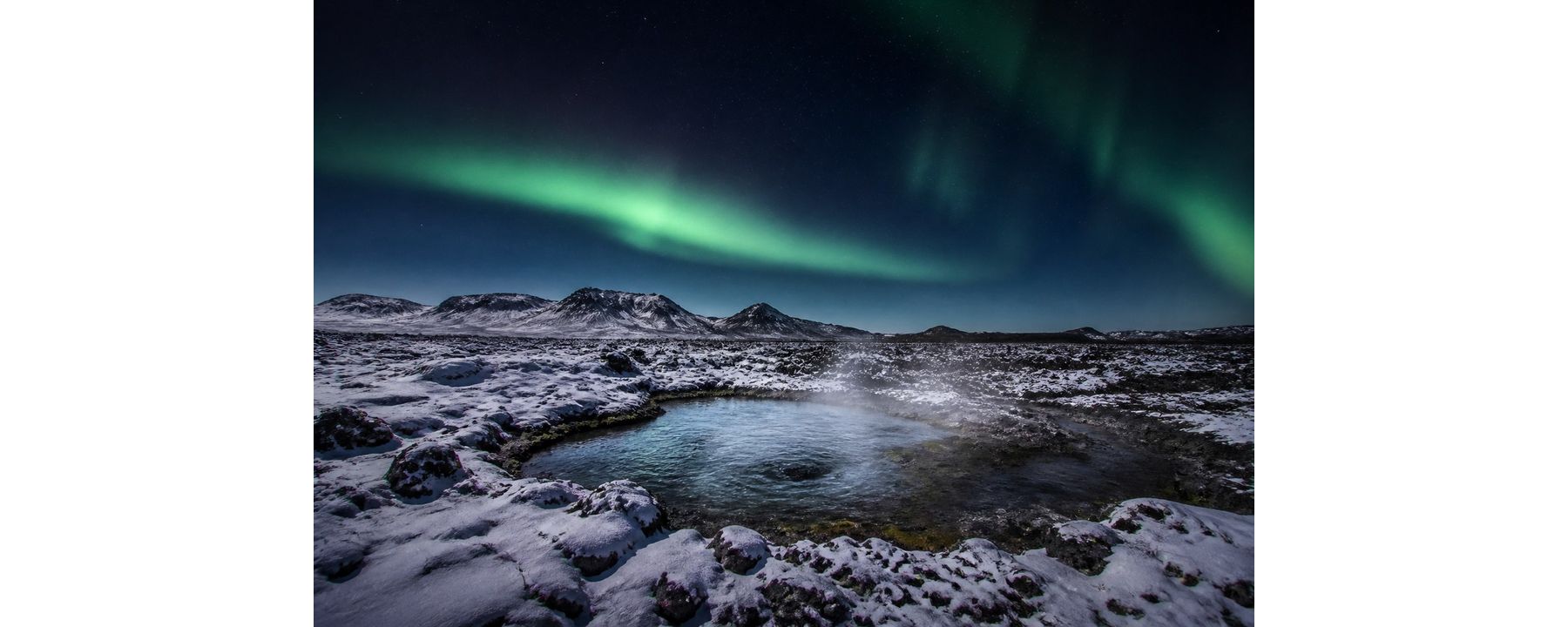 Northern lights over a snowy lava field and a steaming natural pool