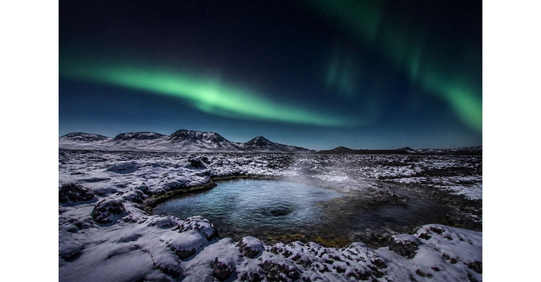 Northern lights above a snowy Icelandic lava field and steaming natural pool