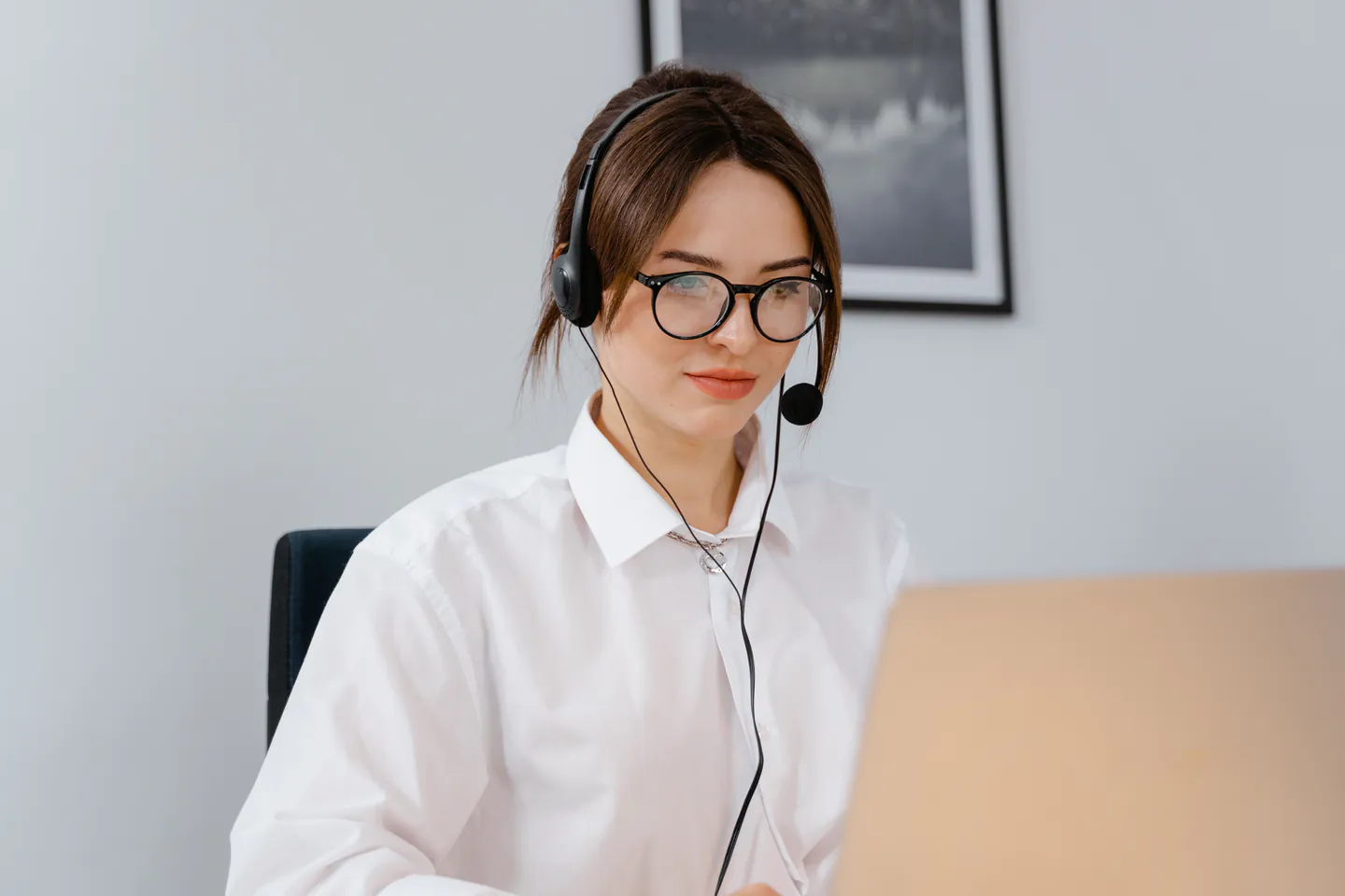 A woman wearing a headset working at a laptop in an office.